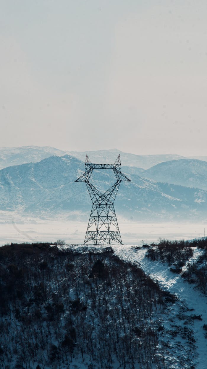 A snow-covered landscape featuring a power line tower against distant mountains.